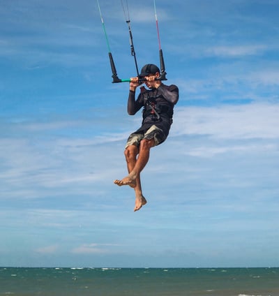 homem pulando de kitesurf na praia.