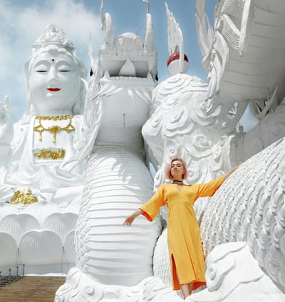 a woman in a yellow dress standing in front of a statue of a dragon