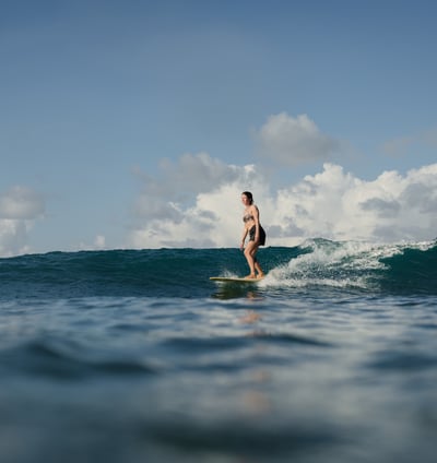 Woman taking surf lessons at a surf school in Kuta Lombok, riding a wave on a sunny ocean day