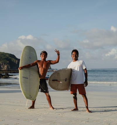Two surf instructors at a surf school in Kuta Lombok holding boards on beach, offering surf lessons.