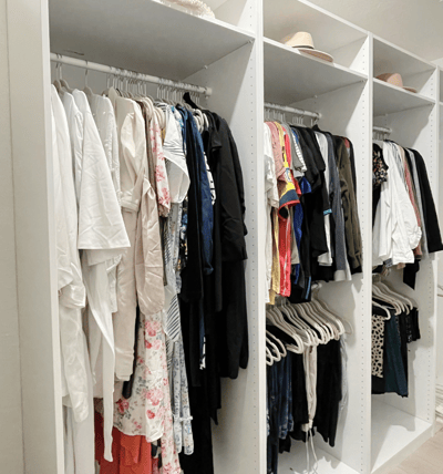 Open closet with color-coded clothing and neatly arranged hangers on white shelving.