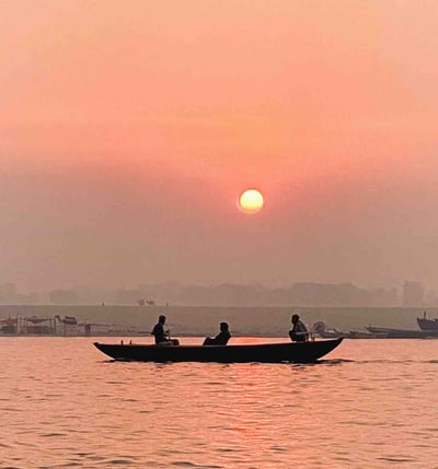 Sunrise over the Ganges River in Varanasi with a boat on the water.