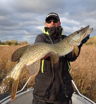 un homme est sur un bateau de pêche , il à pêché un beau brochet avec fishing escape sweden. .