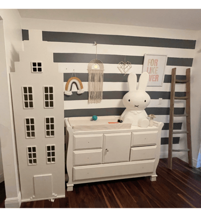Whimsical nursery wall with bold stripes, white dresser, and playful decorative accents.