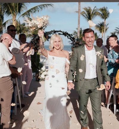 a man and woman walking down a beach wedding ceremony