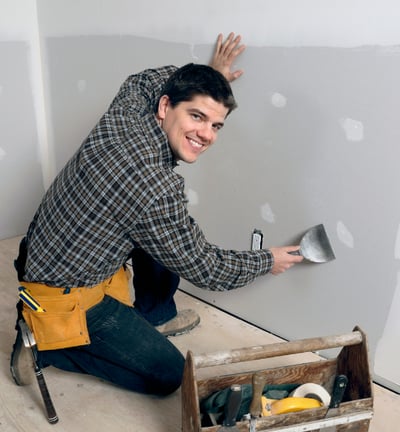 a handy man is smiling and repairing a drywall