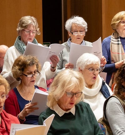 A group of female singers stand in lines holding sheets of music