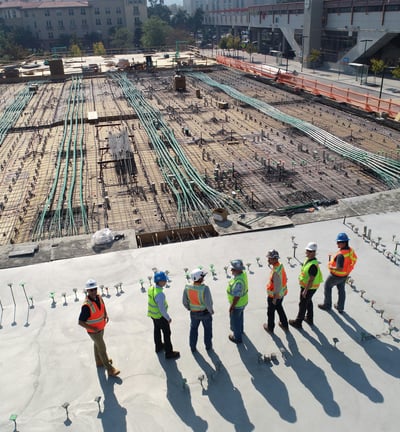 Engenheiros e trabalhadores da construção civil analisando o andamento de uma obra com estrutura de concreto e tubulações exp