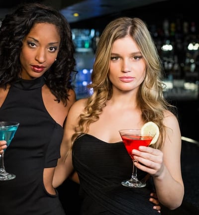 Two stylish women holding colorful cocktails at a sleek Las Vegas bar, showcasing the upscale downtown nightlife vibe.