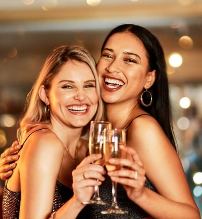Two women laughing and clinking champagne glasses during a vibrant night out in downtown Las Vegas.