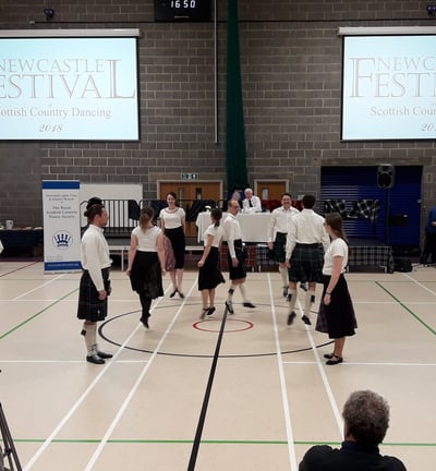 Team in kilts/black skirts and white shirts dancing a pas de basque.