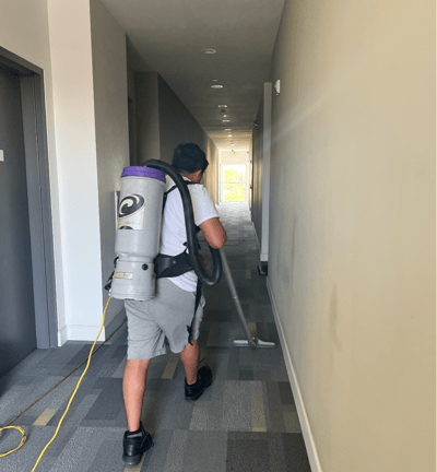a man with a backpack vacuum cleaning the hallway carpet