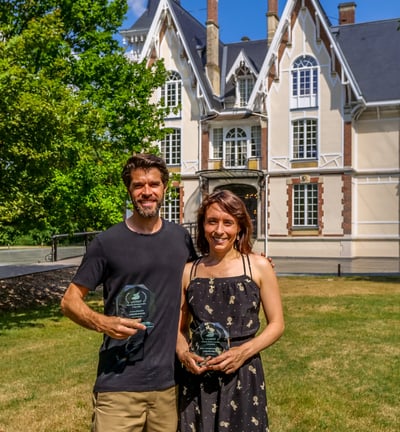 Un homme et une femme qui posent en souriant avec un trophée devant un chateau