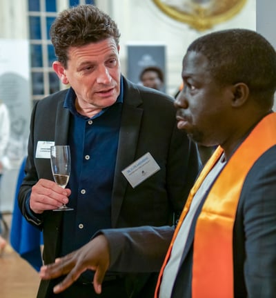 Un homme avec une coupe de champagne qui en regarde un autre et qui discutent