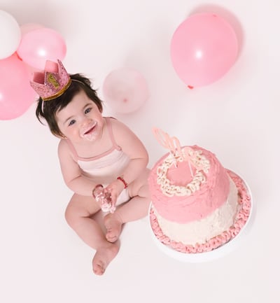 a baby girl sitting near a cake