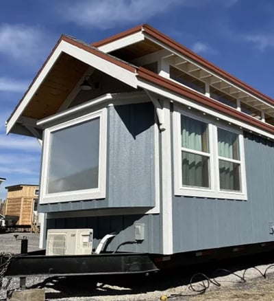 Blue and white tiny home on wheels with large windows