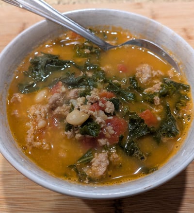 A photo of a bowl of soup, containing ground turkey, kale, tomatoes, and white beans