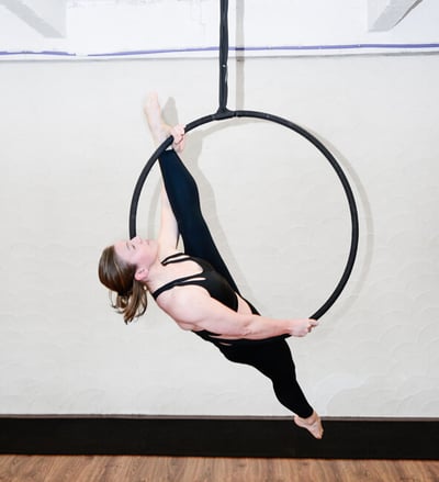 Vrouw in zwarte outfit voert een aerial hoop oefening uit bij De Polecats Fabriek in Gent