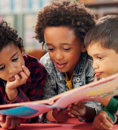 three children are reading a book together in Reno preschool school readiness program