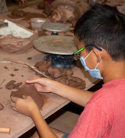 Young boy wearing a mask playing with clay at a table.