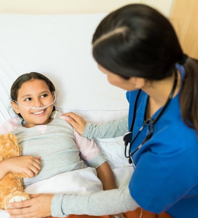 A young girl lies in a hospital bed , receiving care from a female doctor.