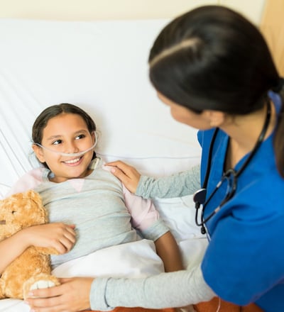 A young girl lies in a hospital bed , receiving care from a female doctor.