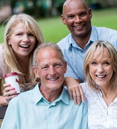 a group of four adults of diverse races sitting on a bench in a park