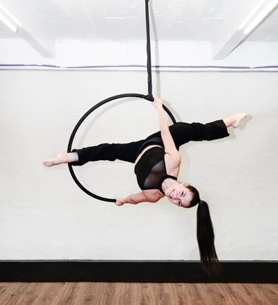 Vrouw in zwarte outfit voert een aerial hoop oefening uit bij De Polecats Fabriek in Gent