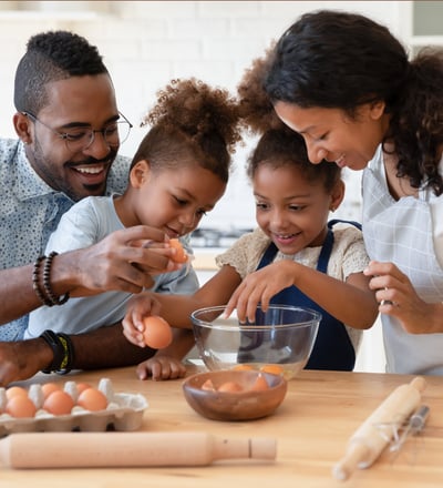 a family breaking eggs as they prepare food together