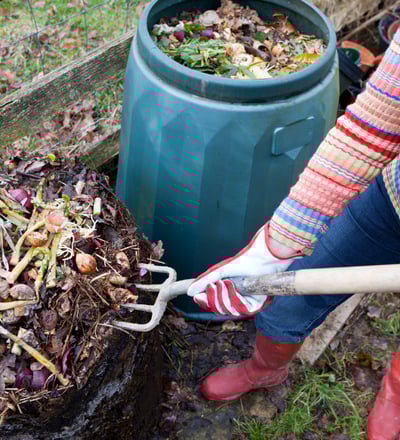 a woman turning over the compost pile