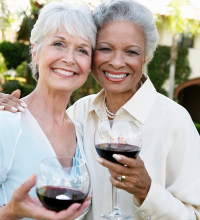 two lovely older women smiling and holding glasses of red wine