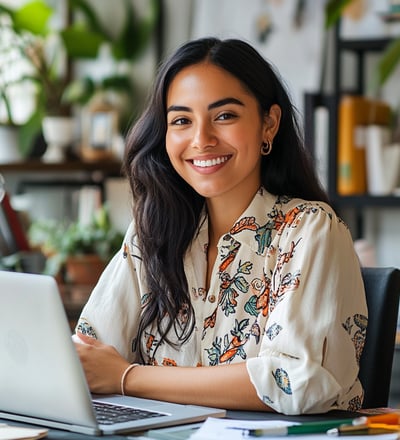 Mujer joven sonriendo enfrente de su laptop, trabajando desde casa y generando ingresos.