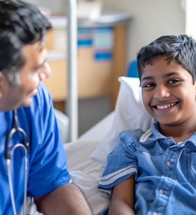 A doctor in blue scrubs is examining a young boy in a hospital bed.