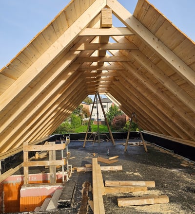 Holzkonstruktion eines Dachstuhls im Rohbau mit Blick auf Wohngebiet im Hintergrund