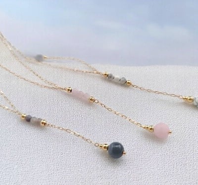 Ensemble de 3 colliers en plaqué or et pierre naturelles, sur du sable 