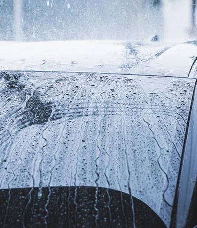 automobilis, kurio priekinis stiklas uždengtas lietumi, bet vanduo varva žemyn dėl hidrofobikos