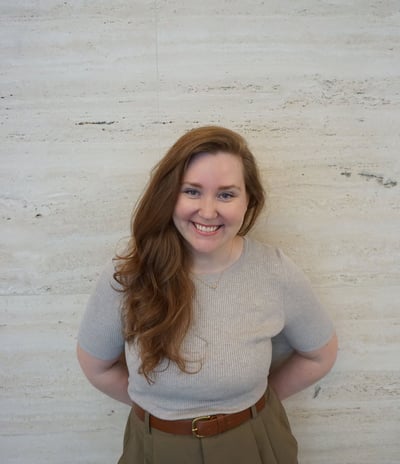 a woman in a gray sweater and brown belted pant