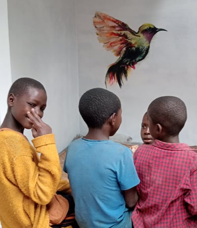 Image of 4 children in front of bird mural, with one looking back at the camera.