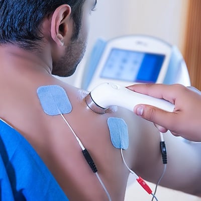 Electrotherapy treatment on session at home for shoulder pain relief using physiotherapy equipment.