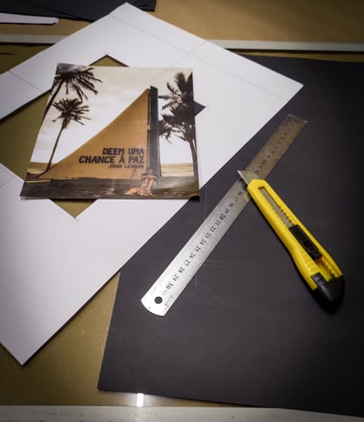 Uma fotográfia sobre uma cartolina e uma régua e um estilete sobre um papel preto