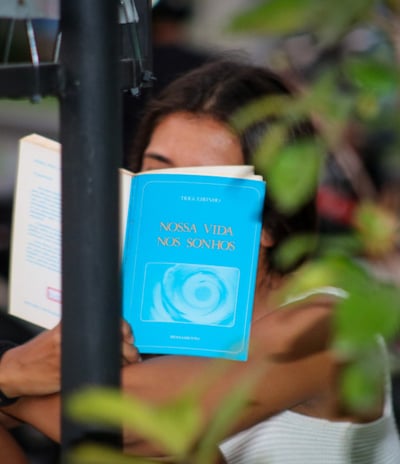 Uma pessoa lendo um livro de capa azul onde o livro tampa seu rosto
