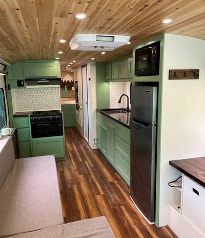 kitchen inside a schoolie bus with a refrigerator, stove, and large sink