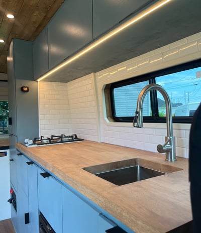 wooden countertop with beautiful backsplash inside van with sink and stovetop