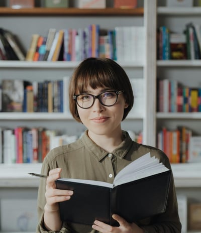 a woman in glasses and a green shirt is holding a book