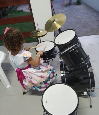 Criança sorridente tocando bateria em uma sala de aula de música, com foco e entusiasmo.