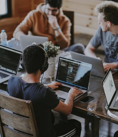 a group of people sitting around a table with laptops