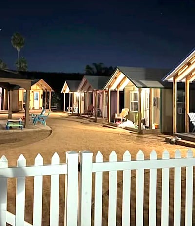 row of hemp town cabins well lit in dusk behind white picket fence