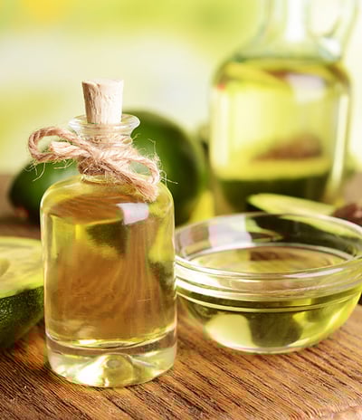 A glass bottle with a cork and twine, filled with a light golden liquid, avocado oil.