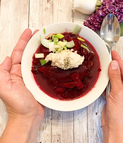 Beet soup in a while bowl with hands holding it