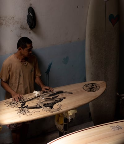 Craftsman shaping a handmade balsa surfboard with intricate artwork